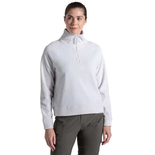A woman modeling a light gray quarter-zip mock neck pullover sweater with dark gray pants, set against a solid beige studio background.