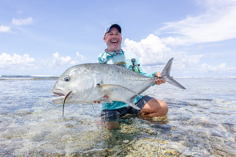 Man holding a large GT fish on a saltwater flat