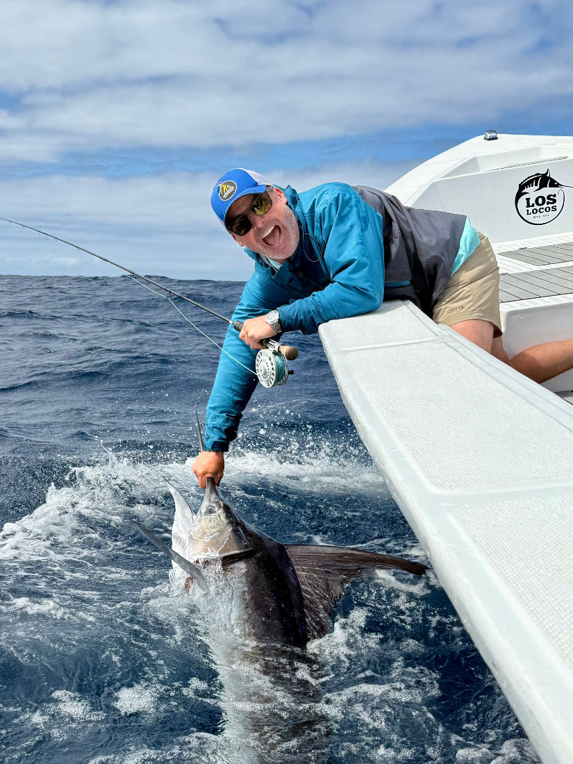 Man on a boat with a large fish, striped  marlin, in the ocean.