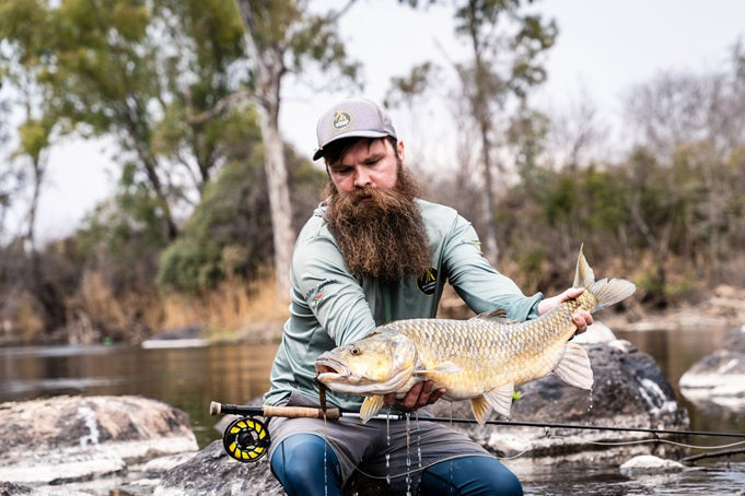 Man holding a large yellowfish on Vaal river with trees in the background